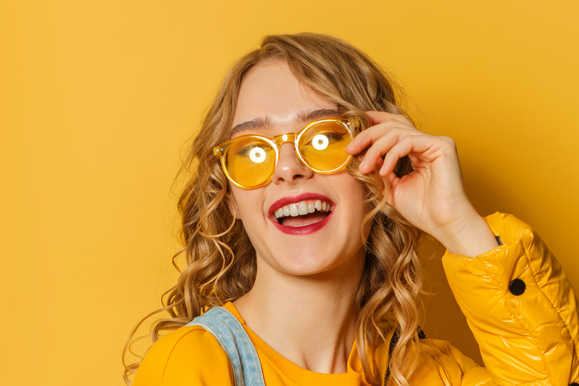 Happy woman wearing sunglasses smiling on yellow background